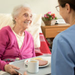 Home caregiver with senior adult woman, serving a meal