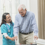 Home healthcare worker helping elderly man with walker