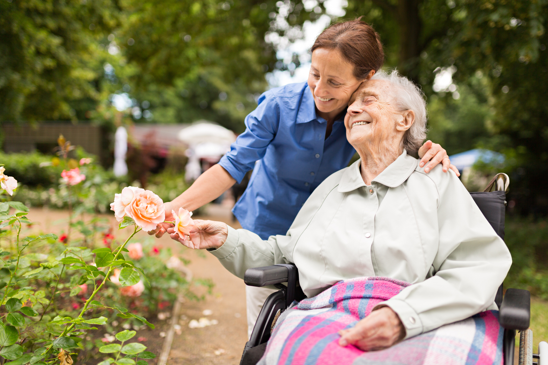 Senior woman sitting on a wheelchair with caregiver, walking in a park