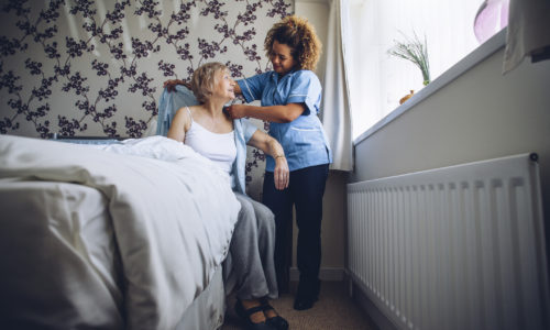 Home Caregiver helping a senior woman get dressed in her bedroom.
