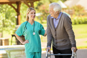 home healthcare nurse talks with her senior male patient. The patient is using a walker. They are on the patio at the man's home.