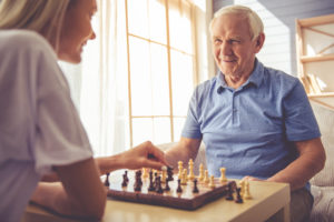 young girl-volunteer and handsome old man are playing chess and smiling
