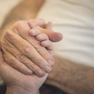 A stock photo of a young woman holding the hands of her Elderly Father who is receiving home hospice care. Photographed using the Canon EOS 1DX Mark II