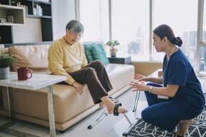 Asian Chinese female physiologist home caregiver encouraging senior woman exercising with her legs cycling