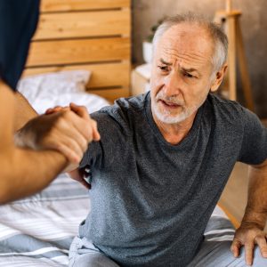 A senior male with white beard getting helped to get up