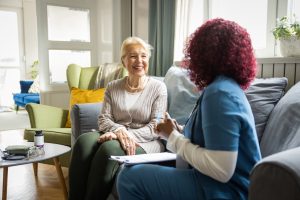 Nurse visiting mature patient at home. She is talking to her about her condition and getting personal information for care.